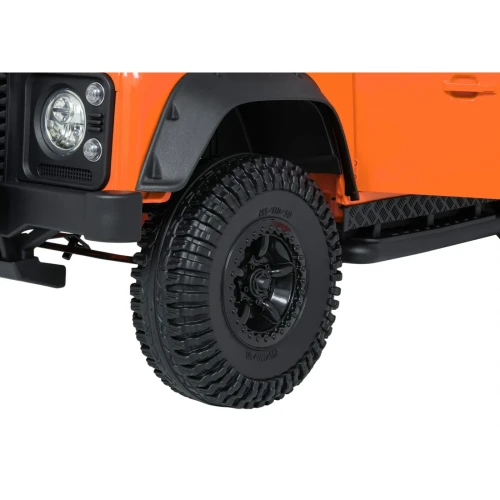Koło z terenową oponą i czarną felgą – zbliżenie pomarańczowego Land Rovera Defender 110 SVX Concept na akumulator dla dzieci.webp