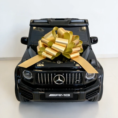 Przód z grillem Panamericana, gwiazdą Mercedesa i złotą kokardą prezentową na masce – czarny Mercedes AMG G63 XXL na akumulator dla dzieci.webp