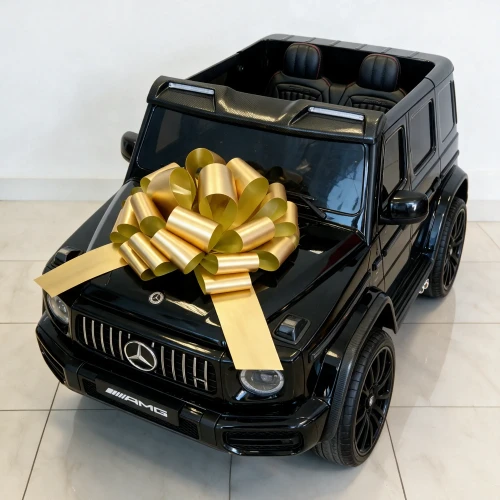 Widok z góry na dwuosobowe wnętrze z fotelami AMG, czarne felgi i złotą kokardę na masce – czarny Mercedes AMG G63 XXL, auto elektryczne na akumulator dla dzieci.webp