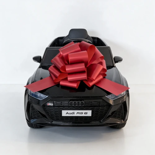 Czerwona kokarda na masce czarnego Audi RS6, widok z przodu na grill i reflektory – samochód na akumulator dla dzieci zapakowany na prezent.webp