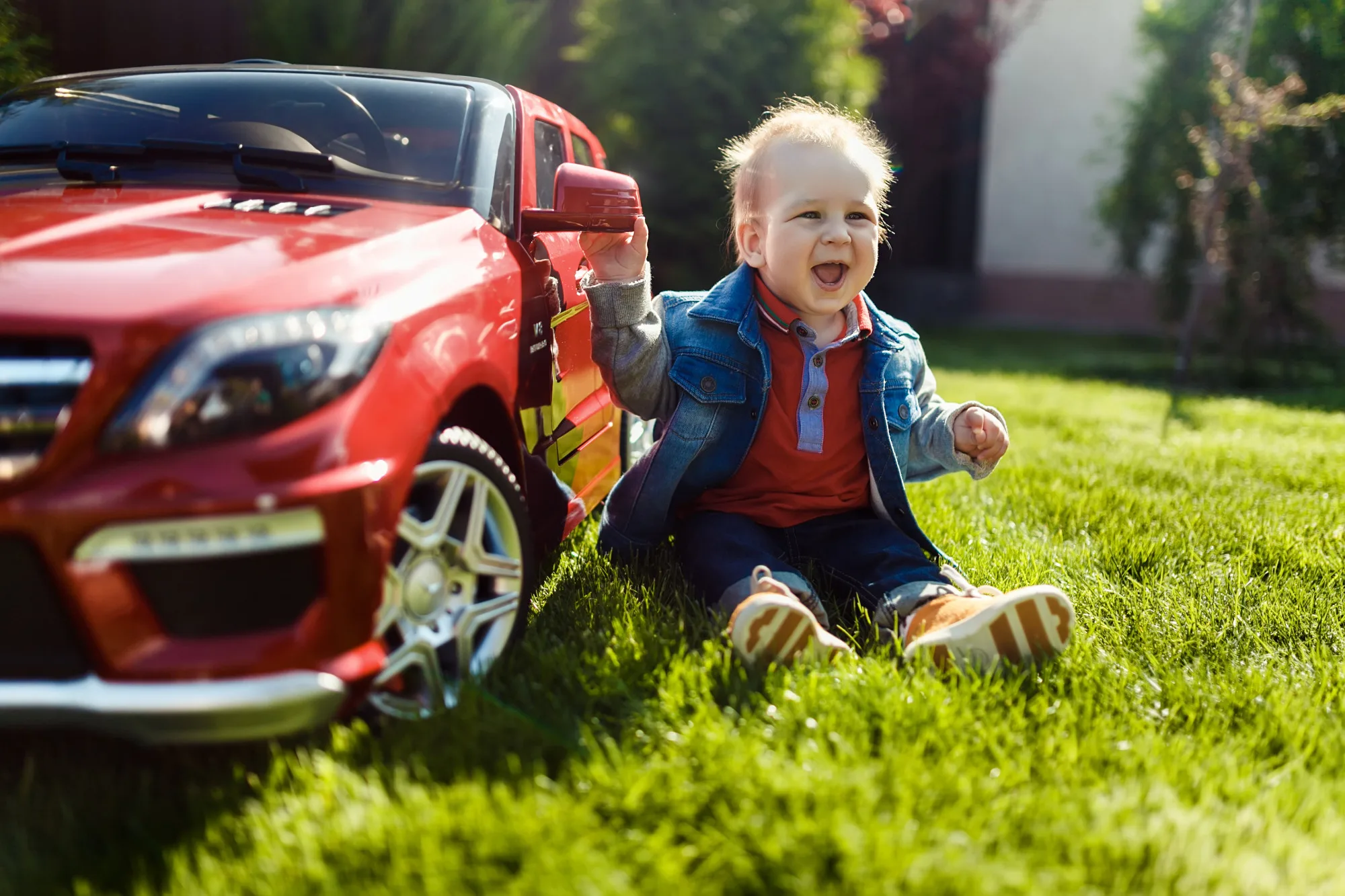 Dziecko siedzące na trawniku bawiące się czerwonym autkiem Mercedes na akumulator - zabawa na świeżym powietrzu